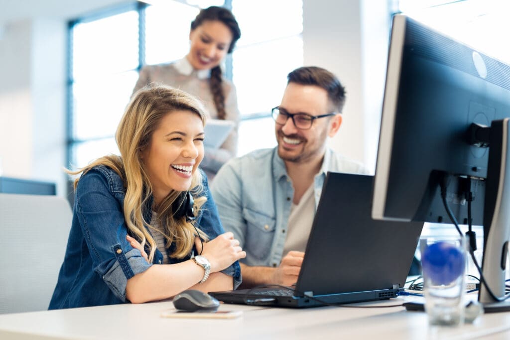 A team at an office computer laughing.